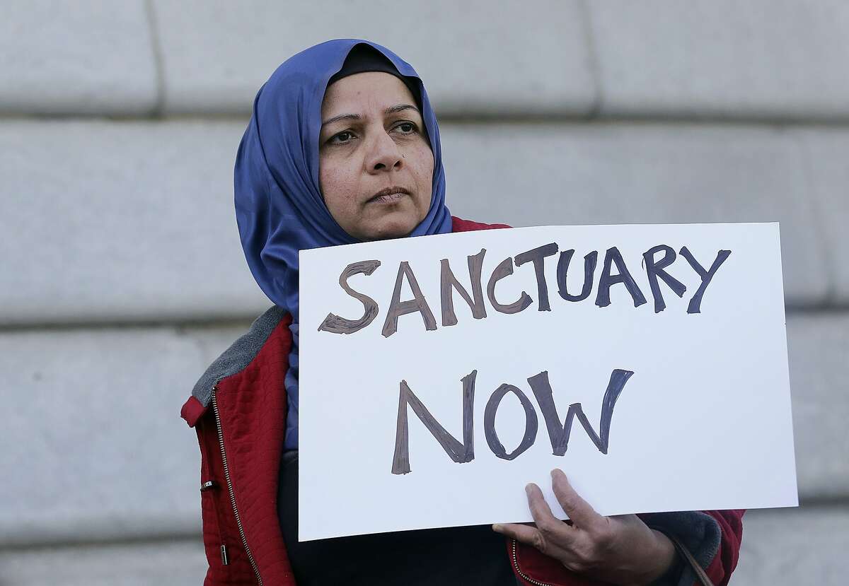FILE - In this Jan. 25, 2017 file photo, a woman holds a sign at a rally outside of City Hall in San Francisco. The Trump administration is moving beyond rhetoric in its effort to crack down on so-called sanctuary cities that refuse to cooperate with federal immigration authorities. The Justice Department is forcing nine communities to prove they are complying with an immigration law to continue receiving coveted law enforcement grant money. (AP Photo/Jeff Chiu, File)