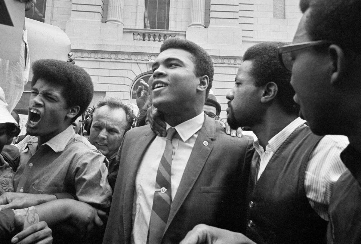 Heavyweight champ Muhammad Ali, center, leaves the Armed Forces induction center with his entourage after refusing to be drafted into the Armed Forces in Houston, April 28, 1967. Hundreds of Ali fans and supporters filled the streets to greet him when he left the building.