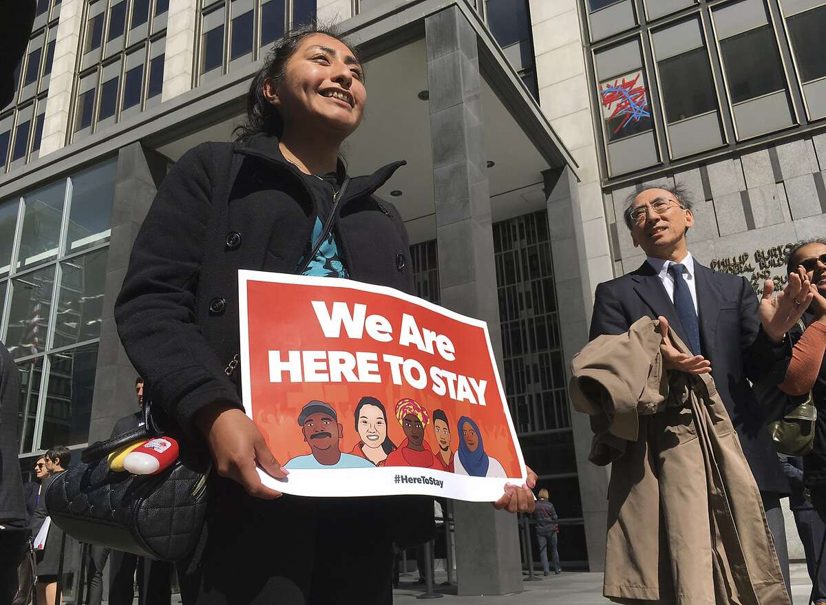 Erica Leyva with the Services, Immigrant Rights and Education Network of San Jose, Calif., carries a sign outside a courthouse where a federal judge heard arguments in the first lawsuit challenging President Donald Trump's executive order to withhold funding from communities that limit cooperation with immigration authorities Friday, April 14, 2017, in San Francisco. An attorney for the U.S. Department of Justice said the executive order withholding funds from sanctuary cities applies to a small pot of grant money, not hundreds of millions of dollars as claimed in lawsuits in California. (AP Photo/Haven Daley)