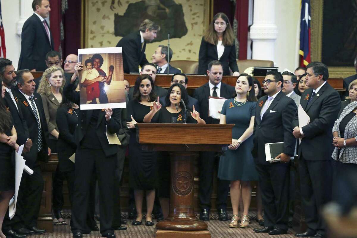 In a slight violation of floor rules, Representative Victoria Neave, Dist 107, presents a photo of her father as she explains her family's plight in entering the United States as members in the House of Representatives debate sanctuary city legislation on April 26, 2017.