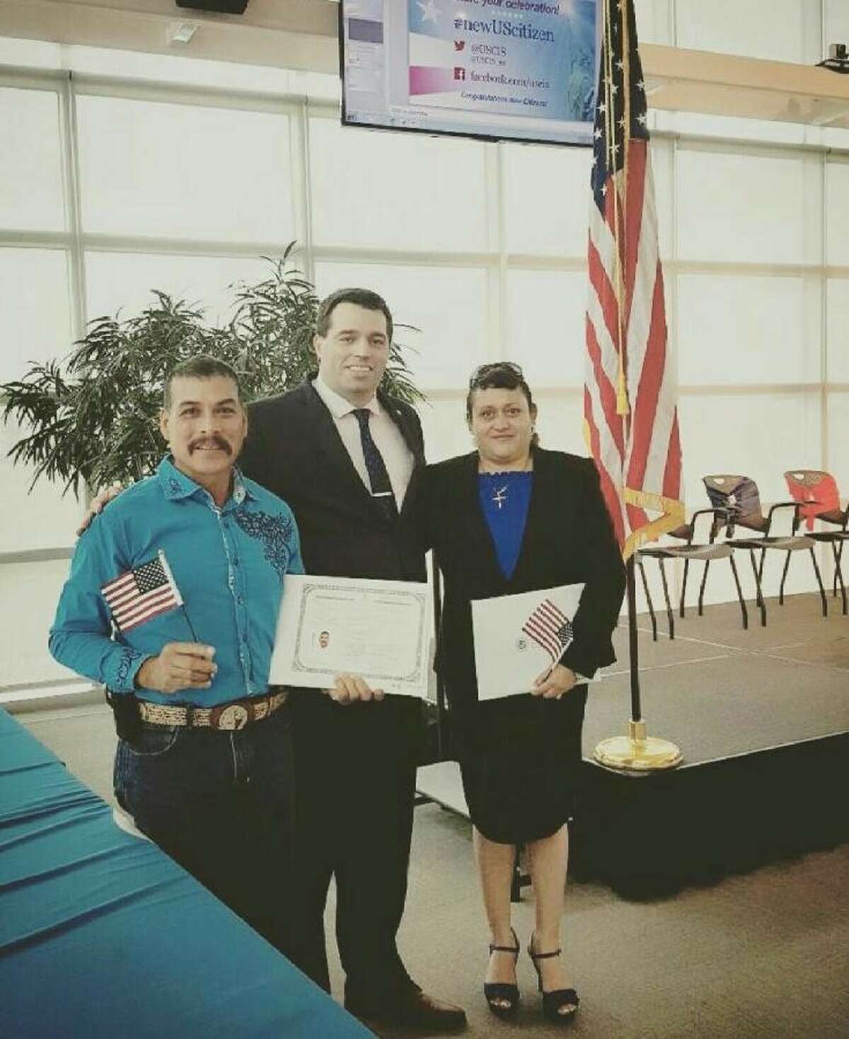 Plainview residents Luis (left) and Maria Martinez hold miniature American flags along with their U.S. citizenship papers after receiving them at a naturalization ceremony April 13 at the U.S. Citizenship and Immigration Services district office in Irving. They are shown with Supervisory Immigration Services Officer Raul Maus.