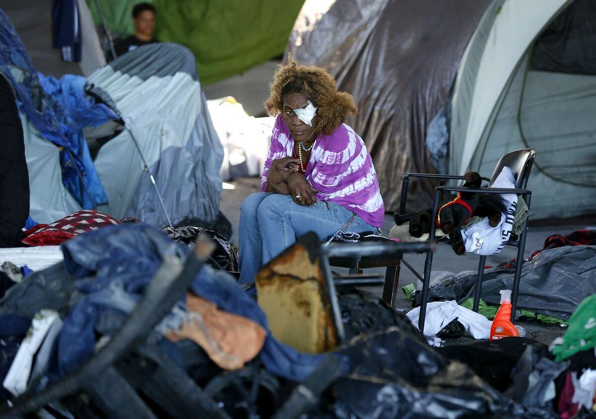 A woman sits with burned items in a homeless encampment at 35th and Peralta streets below Interstate 580 in Oakland, Calif. on Tuesday, May 2, 2017 after a fire torched 20 tents in the city sanctioned camp Monday night.