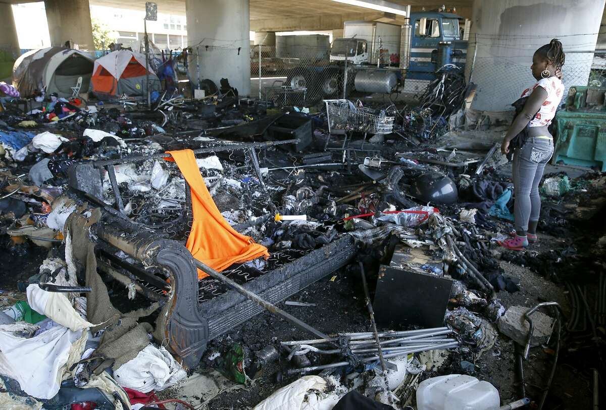 A woman looks at the damage to a homeless encampment at 35th and Peralta streets below Interstate 580 in Oakland, Calif. on Tuesday, May 2, 2017 after a fire torched 20 tents in the city sanctioned camp Monday night.