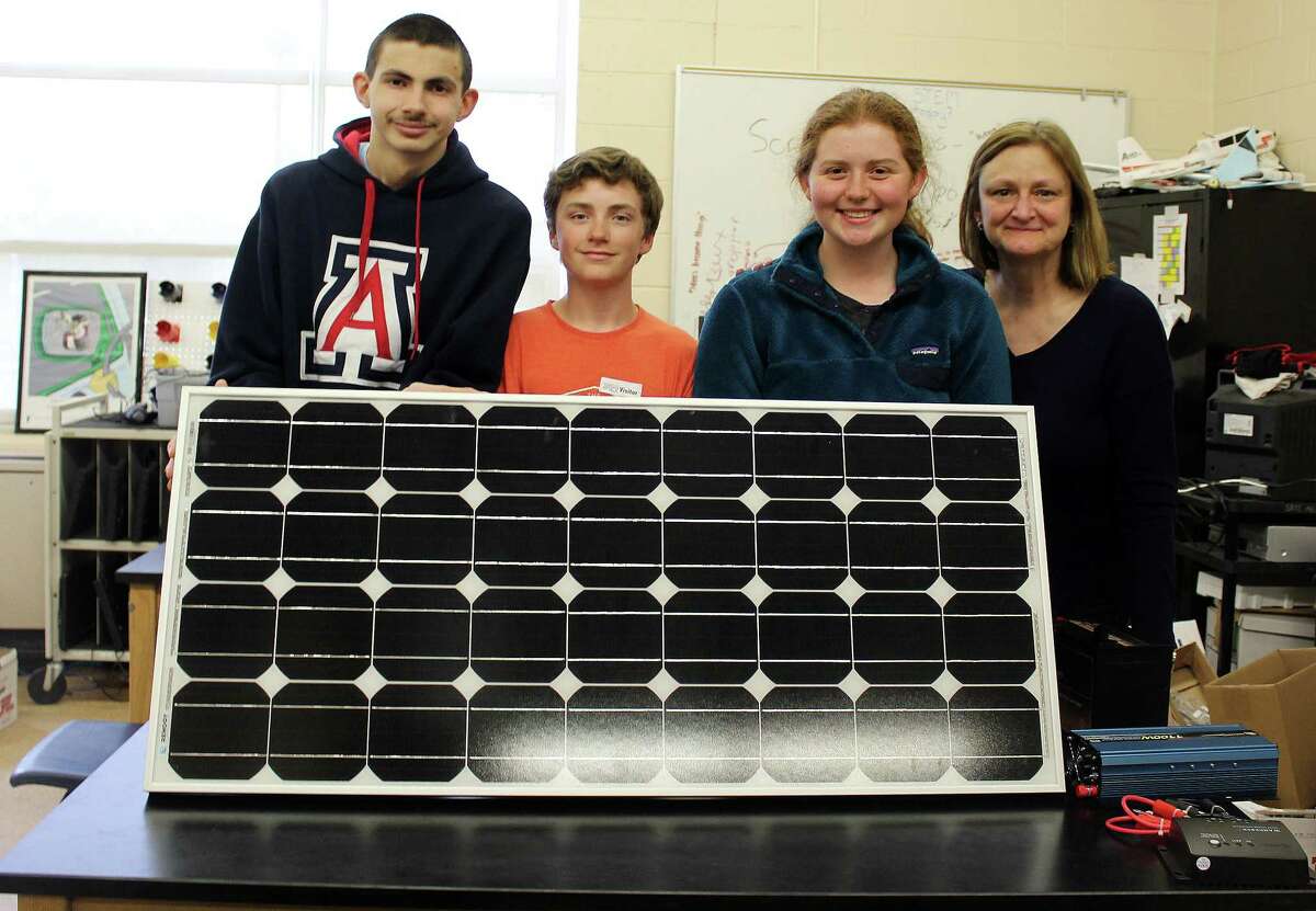 John Renda, left, Shea Smith and Megan Rigione pose with their former teacher, Vivian Birdsall, next to one of the solar panels that will be installed at New Canaan High School thanks to their efforts.