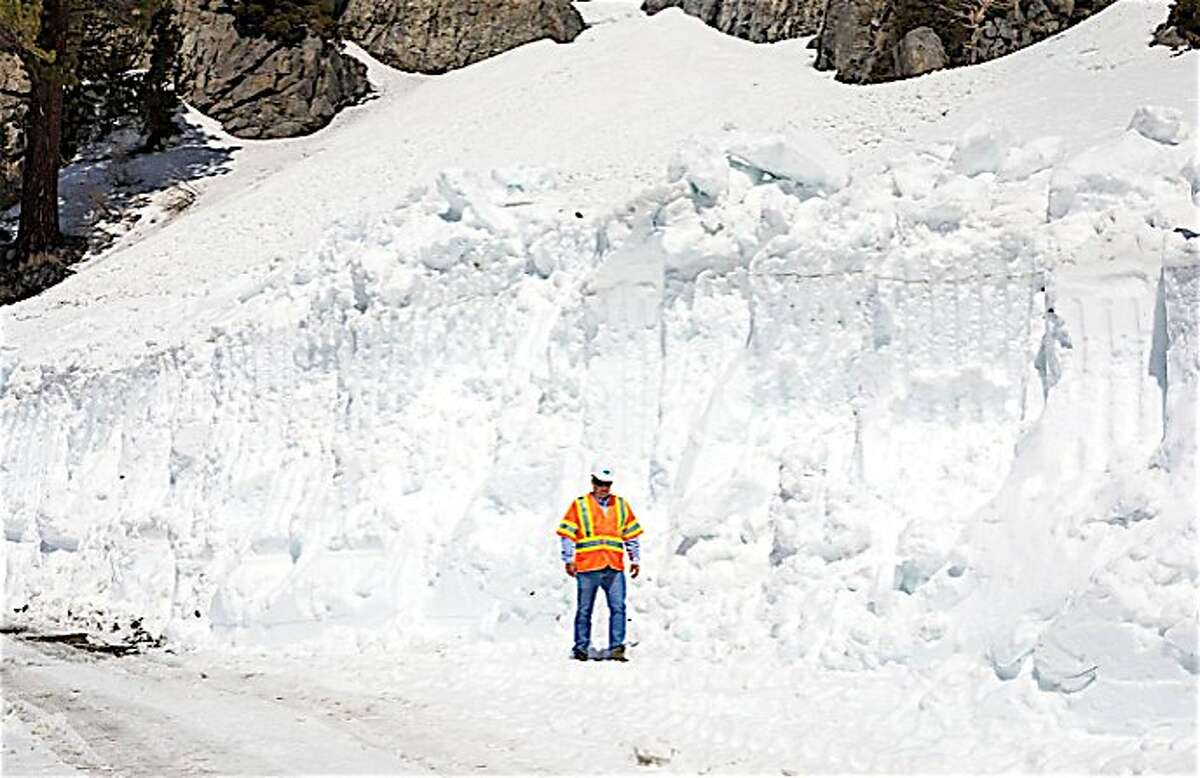 A snow plow crew member stands aside a giant snow drift on Tioga Road/Highway 120, which runs from Crane Flat to Tuolumne Meadows over Tioga Pass in Yosemite National Park