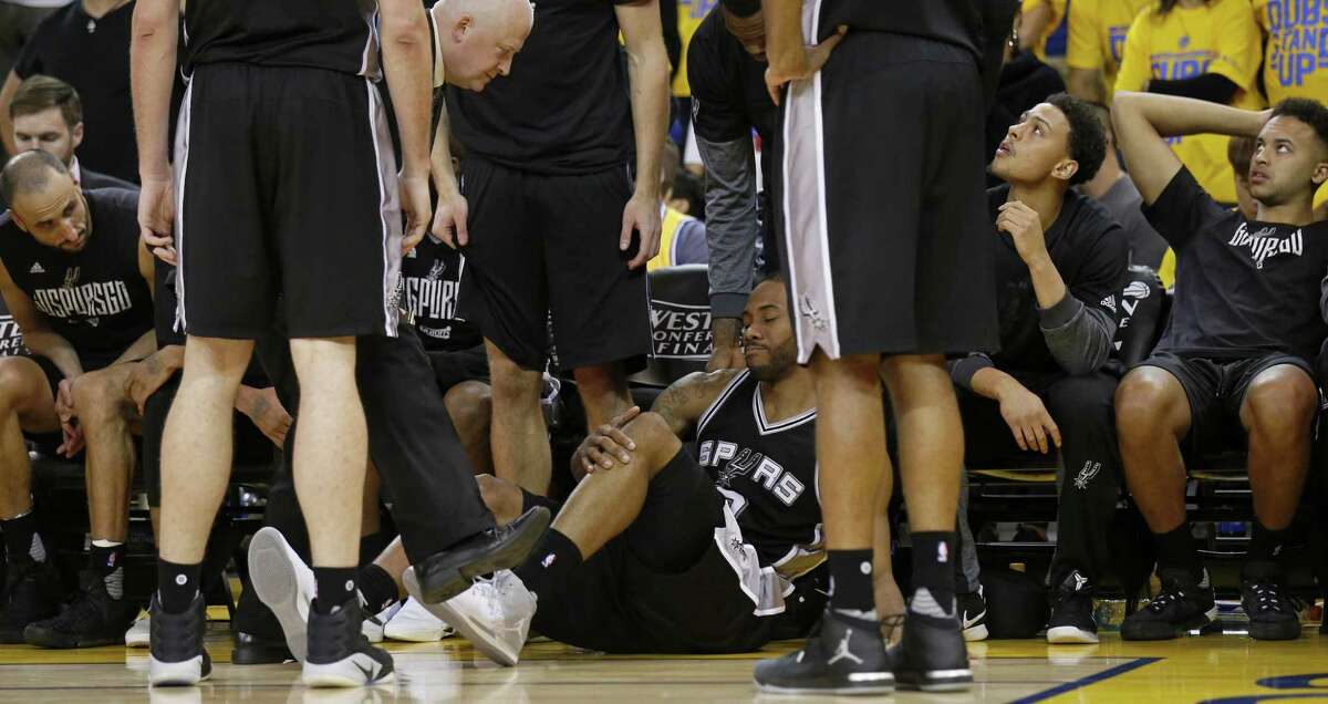 Spurs’ Kawhi Leonard (center) reacts after being injured on a play as head trainer Will Sevening (left) looks on during second half action of Game 1 in the Western Conference finals against the Golden State Warriors on May 14, 2017 at Oracle Arena in Oakland, Calif.