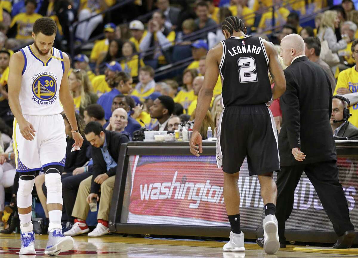 San Antonio Spurs' Kawhi Leonard (center) walks off the court with head athletic trainer Will Sevening (right) as Golden State Warriors' Stephen Curry walks past during second half action of Game 1 in the Western Conference Finals against the Golden State Warriors held Sunday May 14, 2017 at Oracle Arena in Oakland, CA. The Warriors won 113-111.