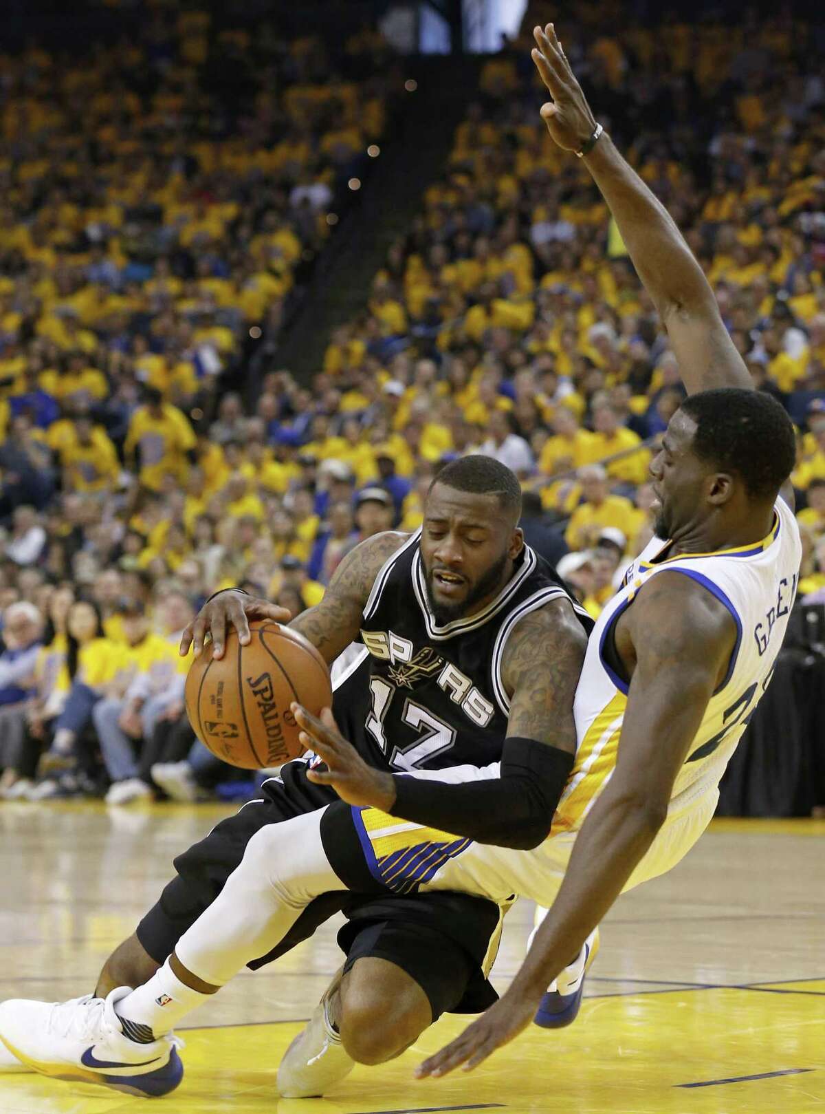 Spurs’ Jonathon Simmons slips as he drives around the Golden State Warriors’ Draymond Green during first half action of Game 1 in the Western Conference finals on May 14, 2017 at Oracle Arena in Oakland, Calif.