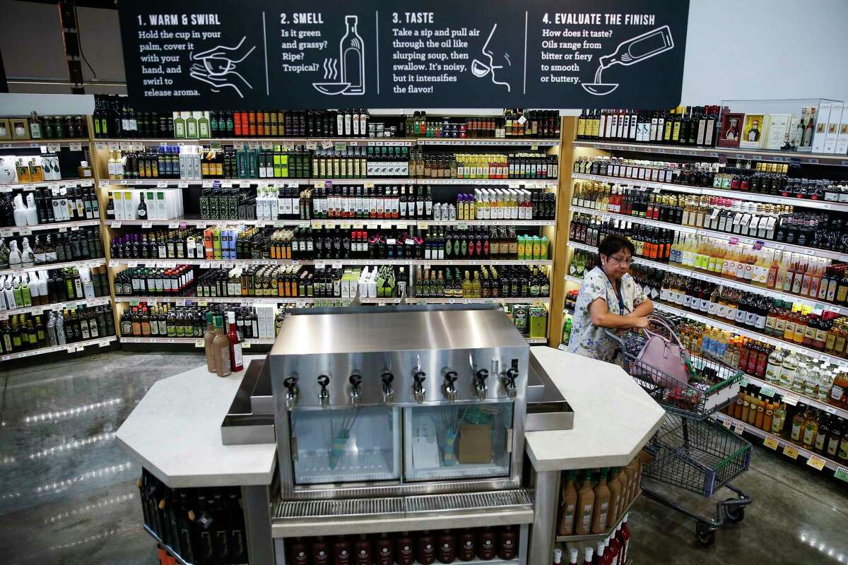 A woman walks past a display olive oil, and the new olive oil tasting station, at Central Market, which recently completed a $10 million renovation.