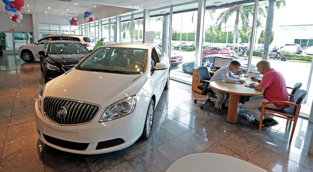 Felipe Perdomo, left, closes a deal with customer John Tsialas at a GMC Buick dealership in Miami. Auto loans are considered part of household debt. ﻿