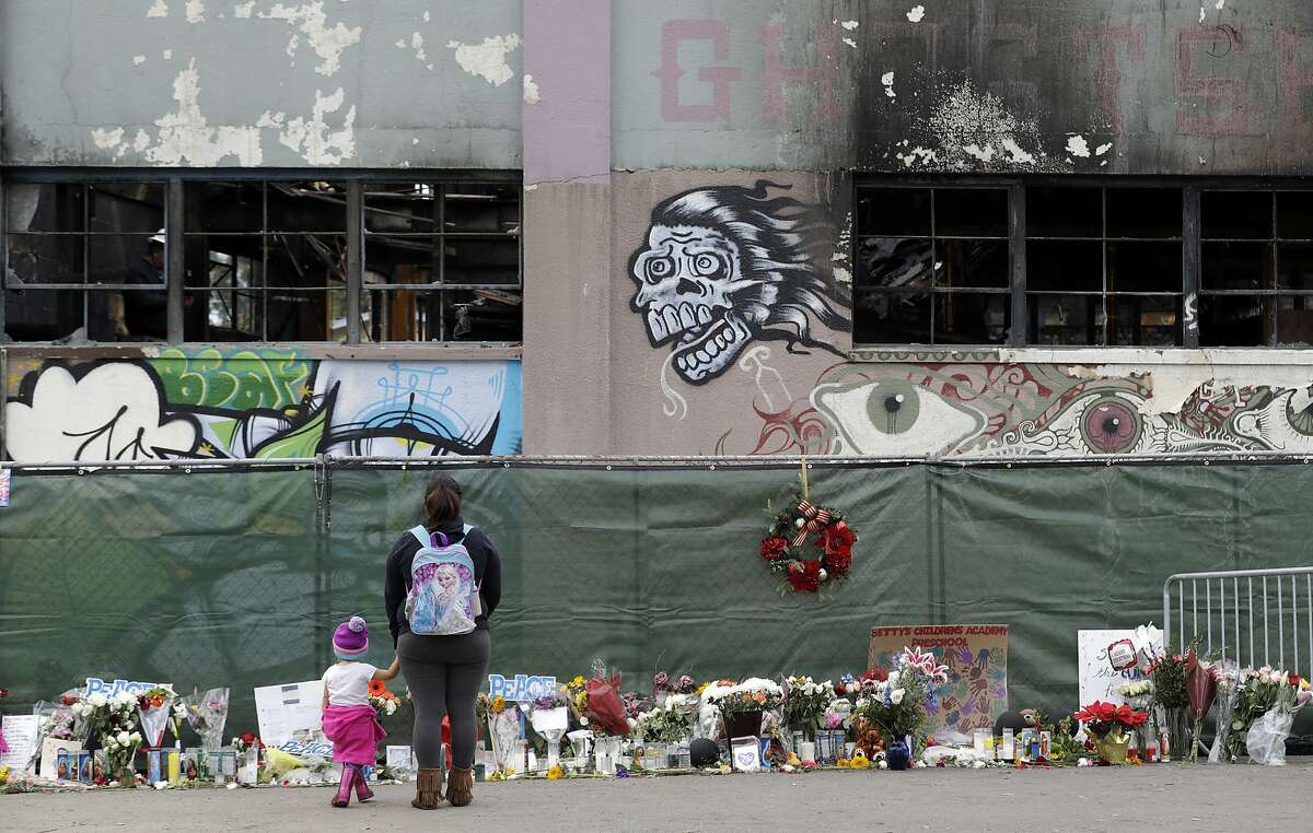 FILE - In this Dec. 13, 2016 file photo, flowers, pictures, signs and candles, are placed at the scene of a warehouse fire in Oakland, Calif. Attorneys representing the families of people who died in the Northern California warehouse fire that broke out during an unlicensed concert plan to file an updated lawsuit against the building's owner and manager Tuesday, May 16, 2017. (AP Photo/Marcio Jose Sanchez, File)
