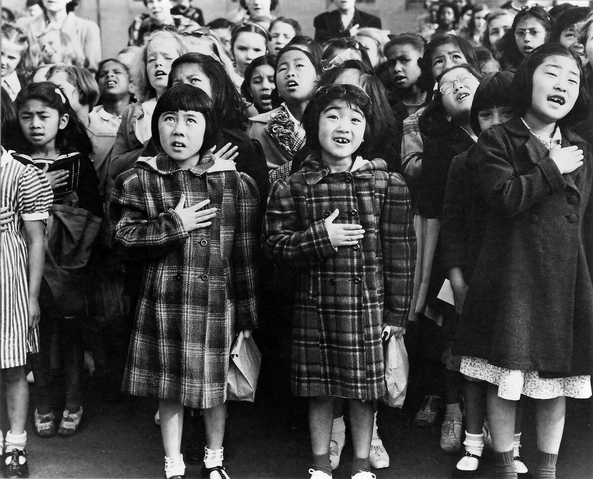 Second generation Japanese Americans Helene Nakamoto Mihara, 7, left, and Mary Ann Yahiro, 7, center, recite the Pledge of Allegiance the Raphael Weill School in San Francisco, California before being sent to the Topaz Internment Camp in Utah in April, 1942. Photograph by Dorothea Lange