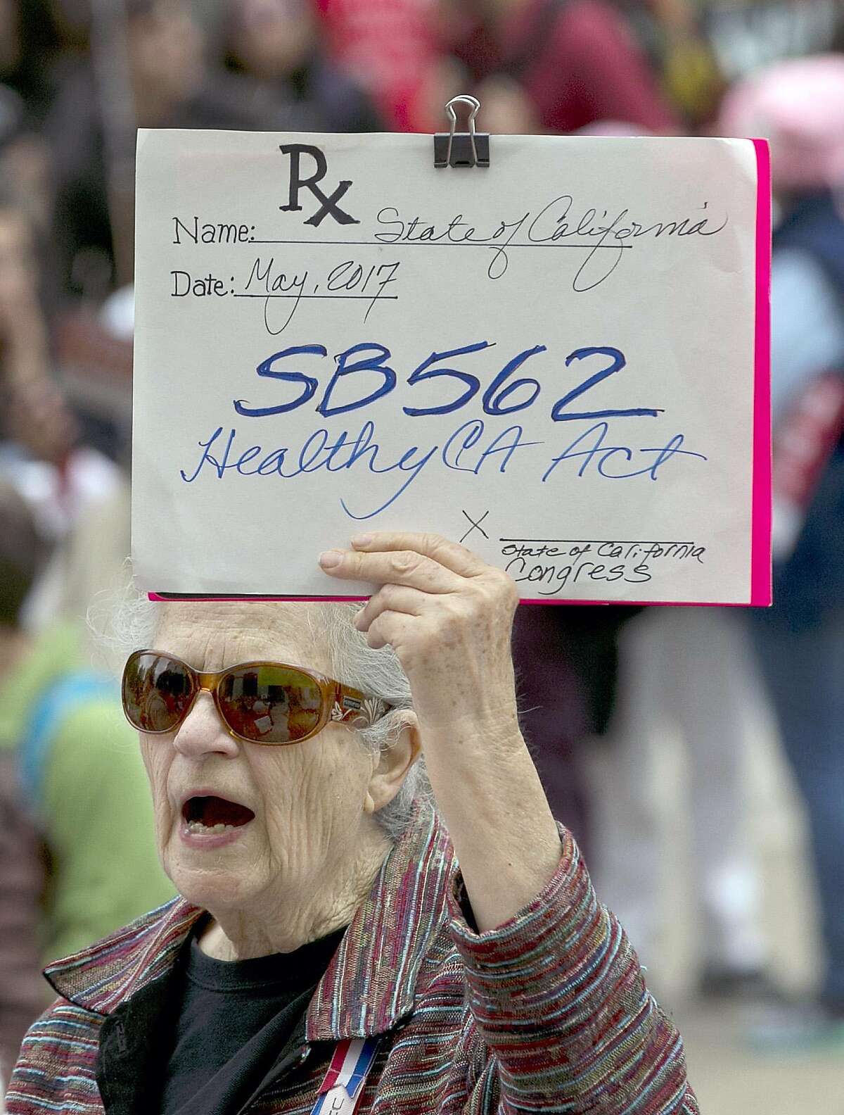 Caroline Elam holds up a mock prescription order calling for passage of SB562, a single-payer health care bill, during a march to the Capitol, Wednesday, April 26, 2017, in Sacramento, Calif. The bill, by Democratic state Sens. Ricardo Lara, of Bell Gardens, and Toni Atkins, of San Diego, would guarantee health coverage with no out-of-pocket cost for all California residents, including people living in the country illegally is to be heard in the Senate Health Committee on Wednesday. (AP Photo/Rich Pedroncelli)