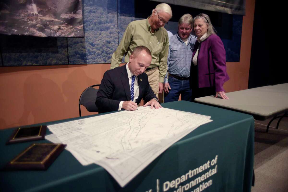 New York State Department of Environmental Conservation (DEC) Commissioner Basil Seggos signs his name to maps that show the new State and private boundaries during an event in the Adirondack Room at the New York State Museum on Monday, May 22, 2017, in Albany, N.Y. The event was held to announce a land agreement that settled a centuries old land dispute between over 200 land owners and the State. Behind him are some of the land owners who were affected by the land dispute. (Paul Buckowski / Times Union)