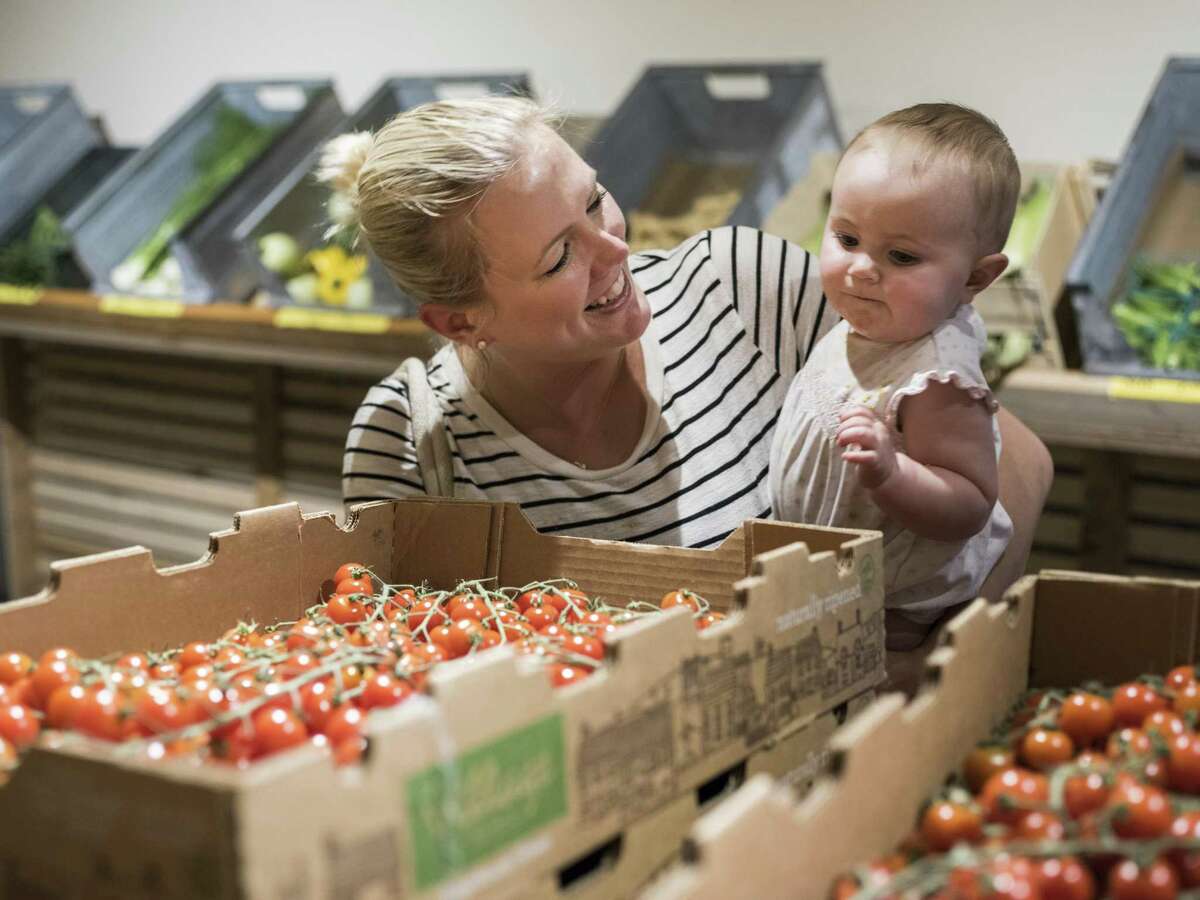 Meg Walker lets her daughter Campbell, 9 months old, pick up a cherry tomato from Trukin' Tomato during the midweek market, a local farmers market generally for wholesalers but open to the public on Wednesdays.