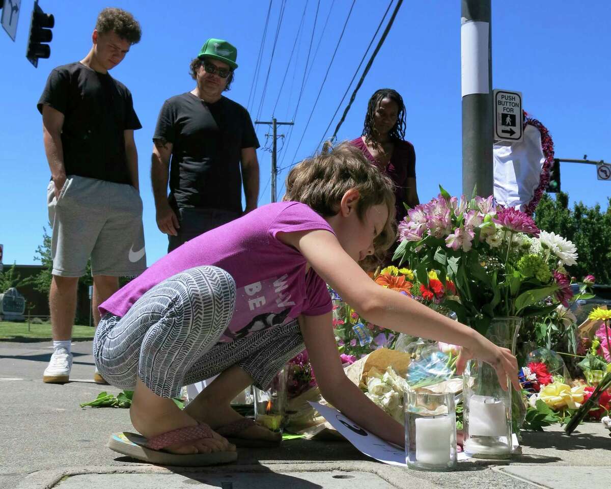 Coco Douglas, 8, leaves a handmade sign and rocks she painted at a memorial in Portland, Ore., on Saturday, May 27, 2017, for two bystanders who were stabbed to death Friday while trying to stop a man who was yelling anti-Muslim slurs and acting aggressively toward two young women. From left are Coco's brother, Desmond Douglas; her father, Christopher Douglas; and her stepmother, Angel Sauls. (AP Photos/Gillian Flaccus)