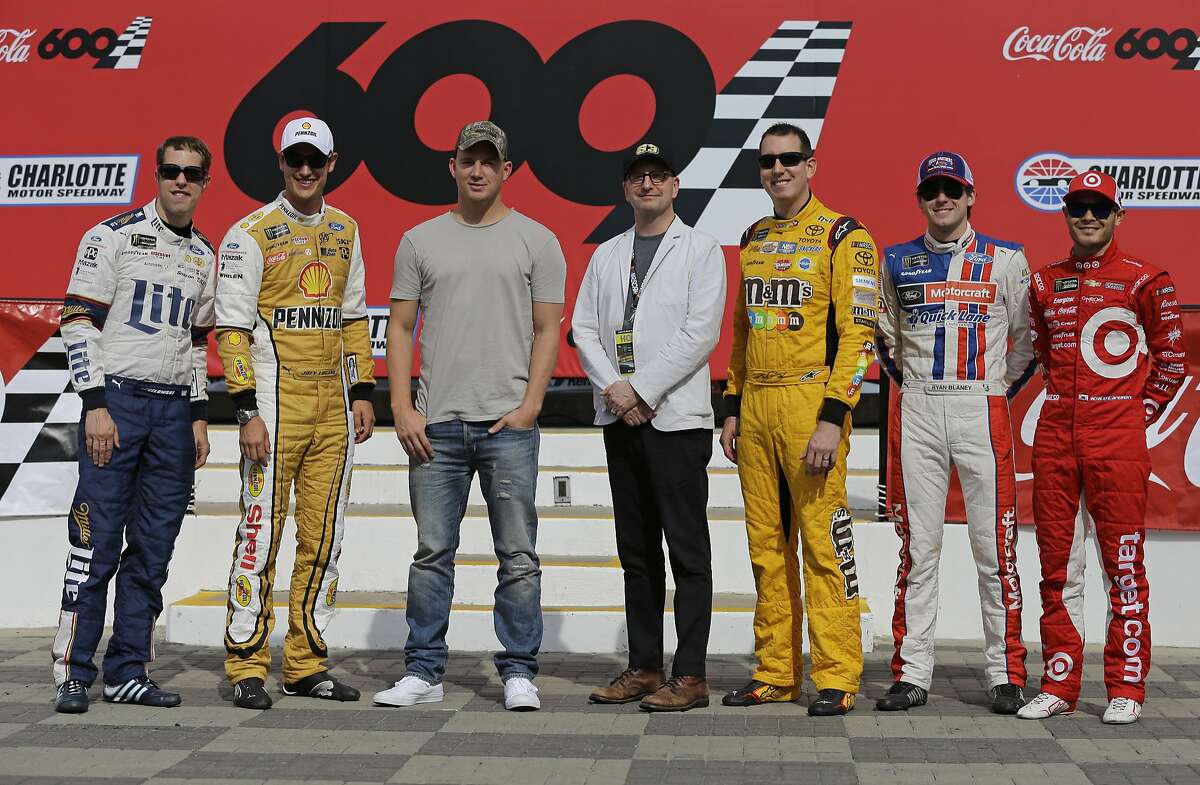 Actor Channing Tatum, third from left, and director Steven Soderbergh, center, pose for a photo with NASCAR drivers, from left to right, Brad Keselowski, Joey Logano, Kyle Busch, Ryan Blaney and Kyle Larson before the NASCAR Cup series auto race at Charlotte Motor Speedway in Concord, N.C., Sunday, May 28, 2017. Tatum and the drivers will star in a new movie filmed at the speedway named "Logan Lucky," and directed by Soderbergh. (AP Photo/Chuck Burton)