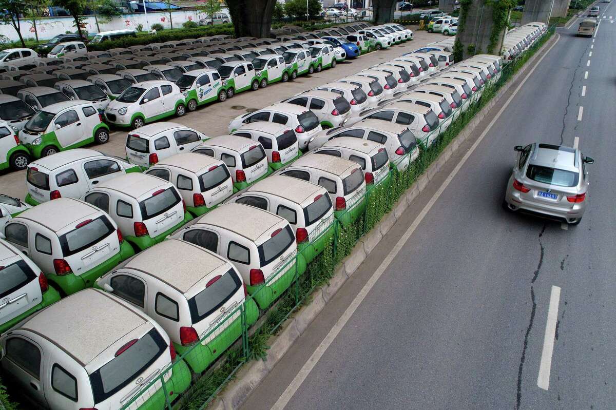 This photo taken on May 22, 2017 shows a car passing new electric vehicles parked in a parking lot under a viaduct in Wuhan, central China's Hubei province. / AFP PHOTO / STR / China OUTSTR/AFP/Getty Images