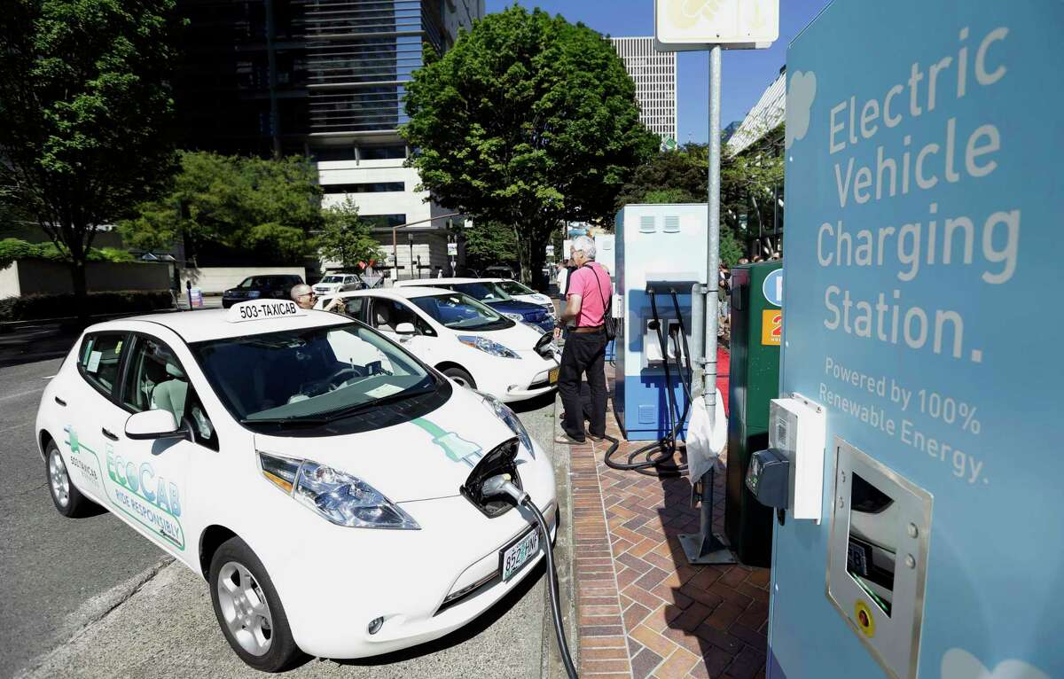 FILE- In this July 28, 2015, file photo a line of electric cars and newly installed charging stations are seen in front of the Portland General Electric headquarters building in Portland, Ore. Texas is again offering rebates to residents who buy electric cars.