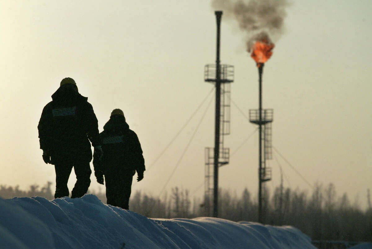Two workers walk near a gas flare-off at the Yukos owned Mamontovskoye oil-field in the Khanty-Mansy region of the Russian Federation, Friday, December 17, 2004. Russia's state-owned OAO Rosneft said it will take over the main production unit of OAO Yukos Oil Co., the exporter of 11 percent of the nation's petroleum. Photographer: Dmitry Beliakov/Bloomberg News.