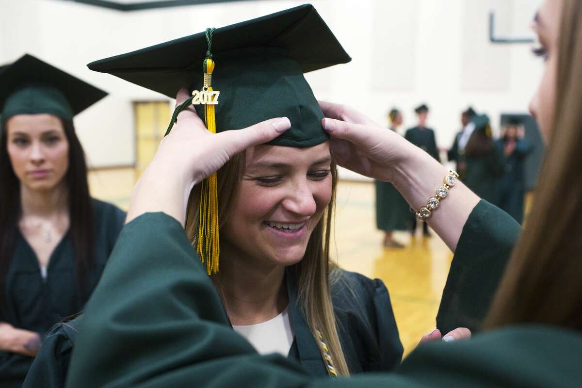 Dow's Lauren McLean helps Caroline Milholland adjust her cap while waiting in the gym before commencement on Friday.