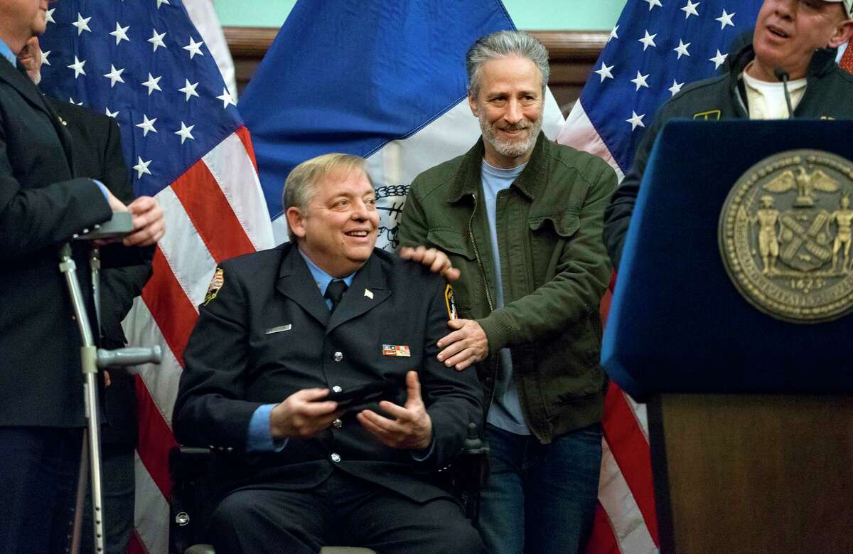 FILE- In this Jan. 9, 2016 file photo, comedian Jon Stewart, right, pats the shoulders of retired FDNY firefighter and Sept. 11 first responder Ray Pfeifer after Pfeifer was given the key to the city at New York's City Hall. Stewart fought back tears Friday, June 2, 2017, during Pfeifer's funeral, as he described his friendship with the retired New York City firefighter who worked in the rescue effort following the Sept. 11 terror attacks. (AP Photo/Craig Ruttle, File) ORG XMIT: NYR101