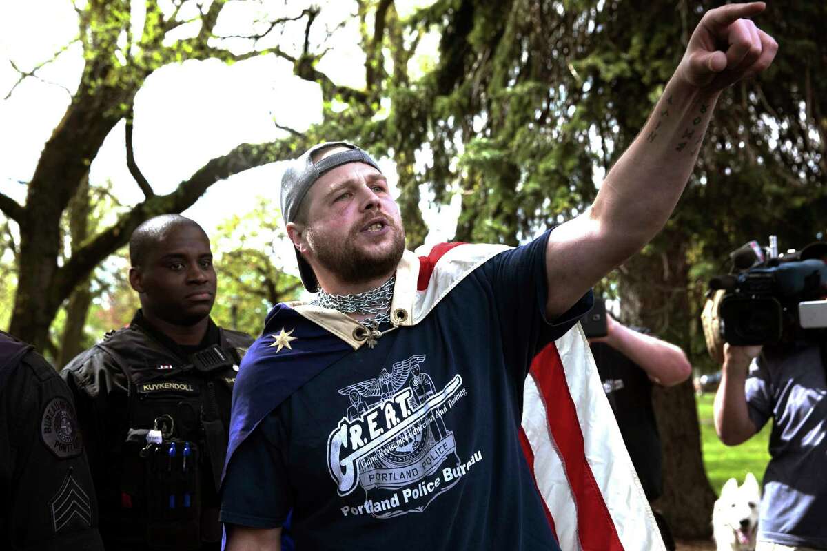 FILE - In this April 29, 2017, file photo provided by John Rudoff, Jeremy Joseph Christian, right, talks during a Patriot Prayer organized by a pro-Trump group in Portland, Ore. Christian, the man accused of stabbing two commuters to death who tried to stop him from hurling anti-Muslim insults at young women on a light-rail train came from a stable family and was a rambunctious teenager who spiraled out of control as he entered his teenage years, according to court records and acquaintances.(John Rudoff via AP, File)