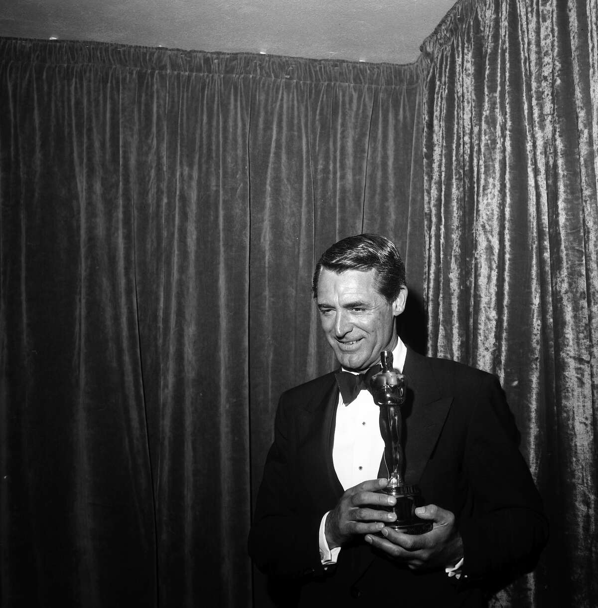 Actors Cary Grant poses with an Oscar for Ingrid Bergman in Los Angeles, 1957.