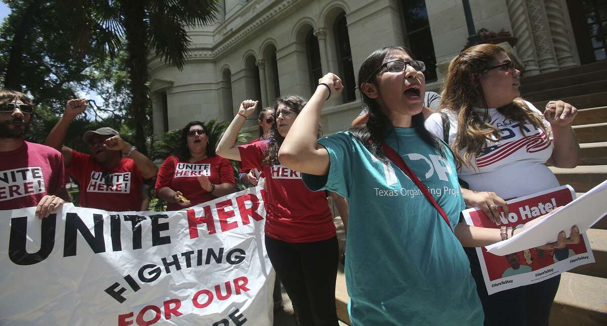 Jessica Azua (right, foreground, arm raised) leads a chant Thursday June 1, 2017 during an announcement made in front of city hall regarding a lawsuit over Senate Bill 4. Senate Bill 4 allows police officers to question a person?’s immigration status during a detainment.