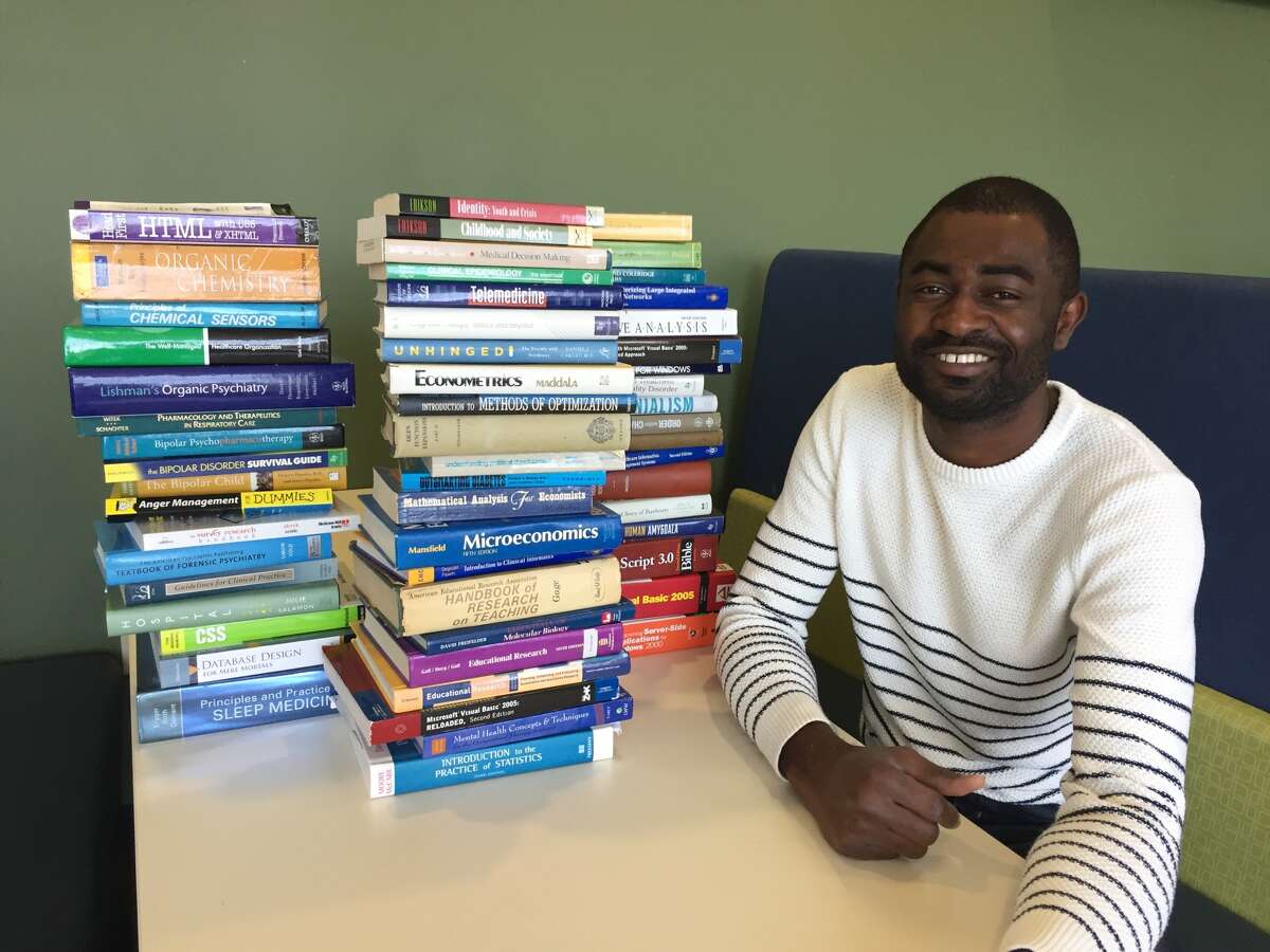 Graduate student Philip Alabi poses next to stacks of donated textbooks that have been collected through his non-profit organization EFIWE.