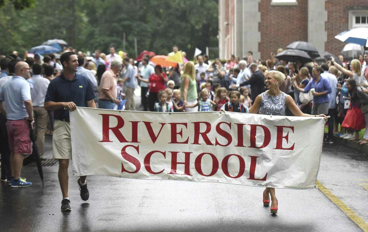 Teachers hold a banner as students follow behind during the Parade of Learners on the first day of school at Riverside School.
