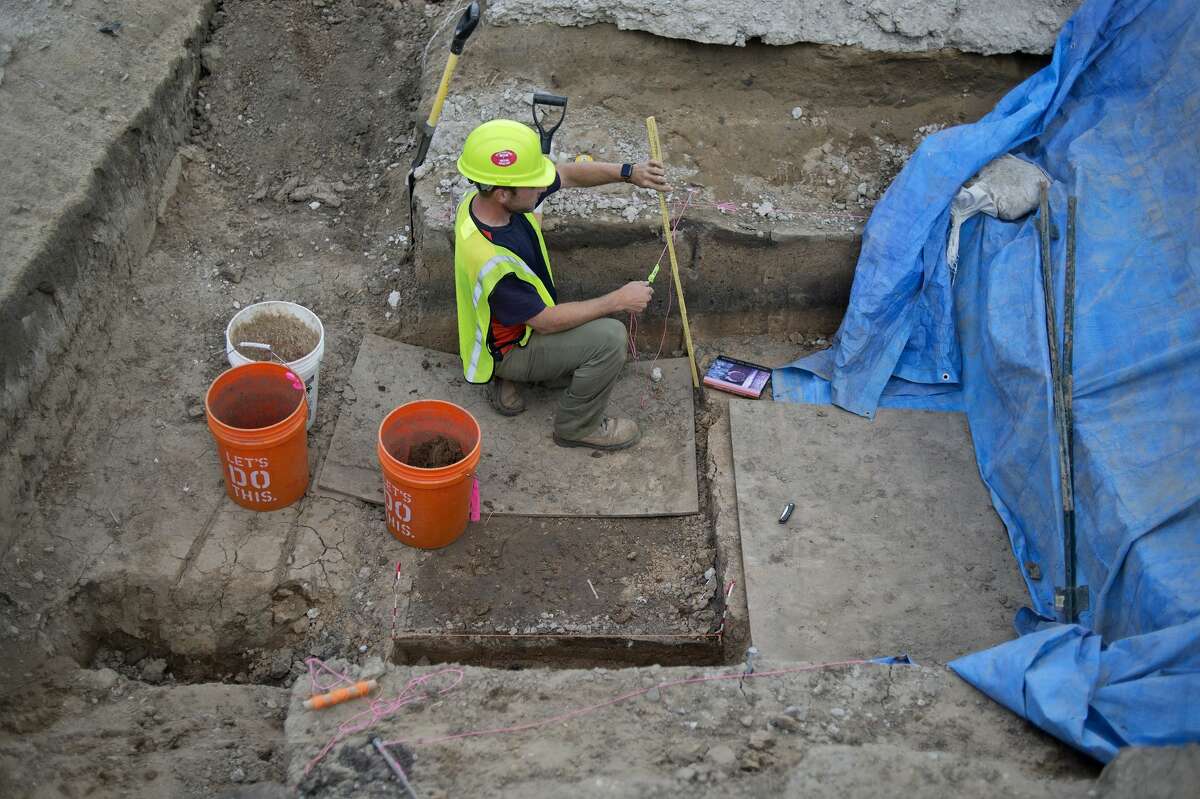 ASC Group employee Kyle Mayer measures the depth of one of the features at the archaeological site near the M-20 bridge Tuesday afternoon.