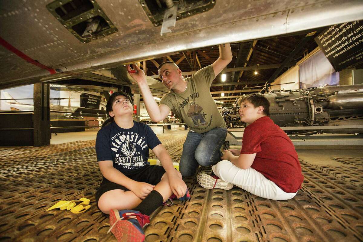 Staff Sgt. Nic Hoefer shows stepsons Reece Zuniga, 13, (left) and Ramsey Zuniga, 11, how to make the template panels as they work on restoring an F-84E Thunderjet at the Texas Military Forces Museum in Austin.