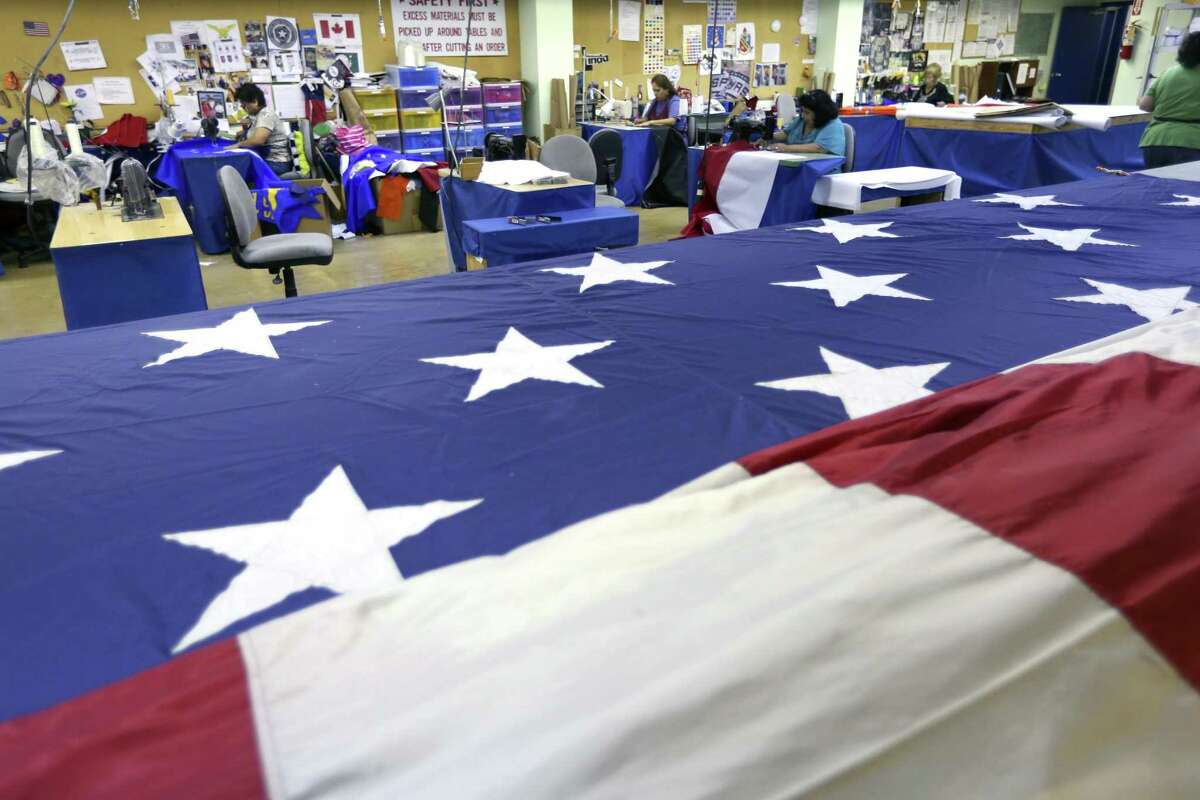 A large American flag being repaired at Dixie Flag & Banner dwarfs the company's seamsters, background. Dixie Flag & Banner has made traditional and custom flags in the San Antonio area for more than 58 years.