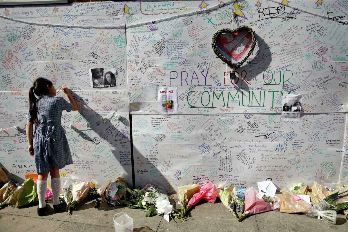 A school girl writes a message on a wall for the victims and in support for those affected by the massive fire in Grenfell Tower, in London, Thursday, June 15, 2017. A massive fire raced through the 24-story high-rise apartment building in west London early Wednesday. (AP Photo/Alastair Grant)