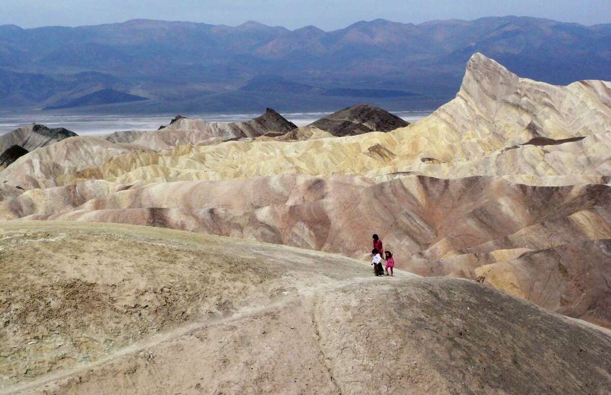 Tourists walk along a ridge at Death Valley National Park, where temperatures could reach 124 this week as a sweltering system envelopes much of the region.