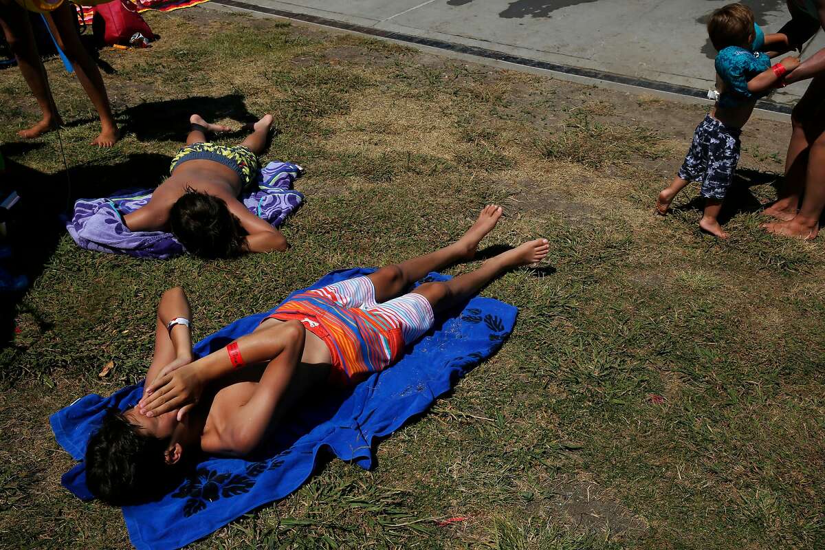 Julian Schmilinsky, 13, lower left, wipes sweat from his face while laying in the sunshine with John-Paul Schmilinsky, 12, upper left, while Heather Mu�oz, far right, picks up her son Leo, 2, as they wait to get back into the Contra Loma Swim Lagoon in the 100 degree heat June 21, 2017 in Antioch, Calif.