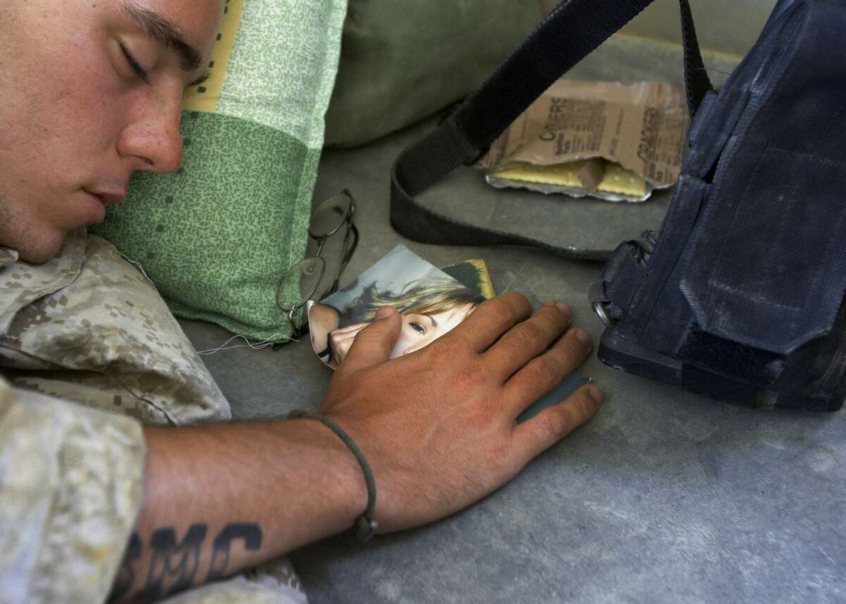 U.S. Marine Lance Cpl. Jeremiah Crosby, 20, of Alamogordo, New Mexico, from Lima Company of the 3rd Battalion, 25th Regiment from Ohio, sleeps with his hand on a picture of his wife, Kandice Crosby, during a lull in the fighting in Parwana, near Haditha, Iraq, Friday, Aug. 5, 2005. A roadside bomb nearby killed 14 Marines, many from this platoon, and a civilian interpreter, in the deadliest roadside bombing suffered by American forces in the Iraq war. (AP Photo/Jacob Silberberg)