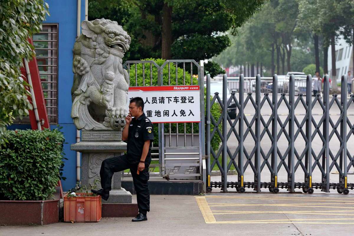 In this June 18, 2017, photo, a security guard smokes near a main entrance gate of the Ganzhou Huajian International Shoe City Co.'s factory, which has made shoes for the Ivanka Trump brand, in Ganzhou in southern China's Jiangxi Province. The sign reads "visitors please exit the vehicle and register, people without relevant reasons cannot enter this important factory area." (AP Photo/Andy Wong)
