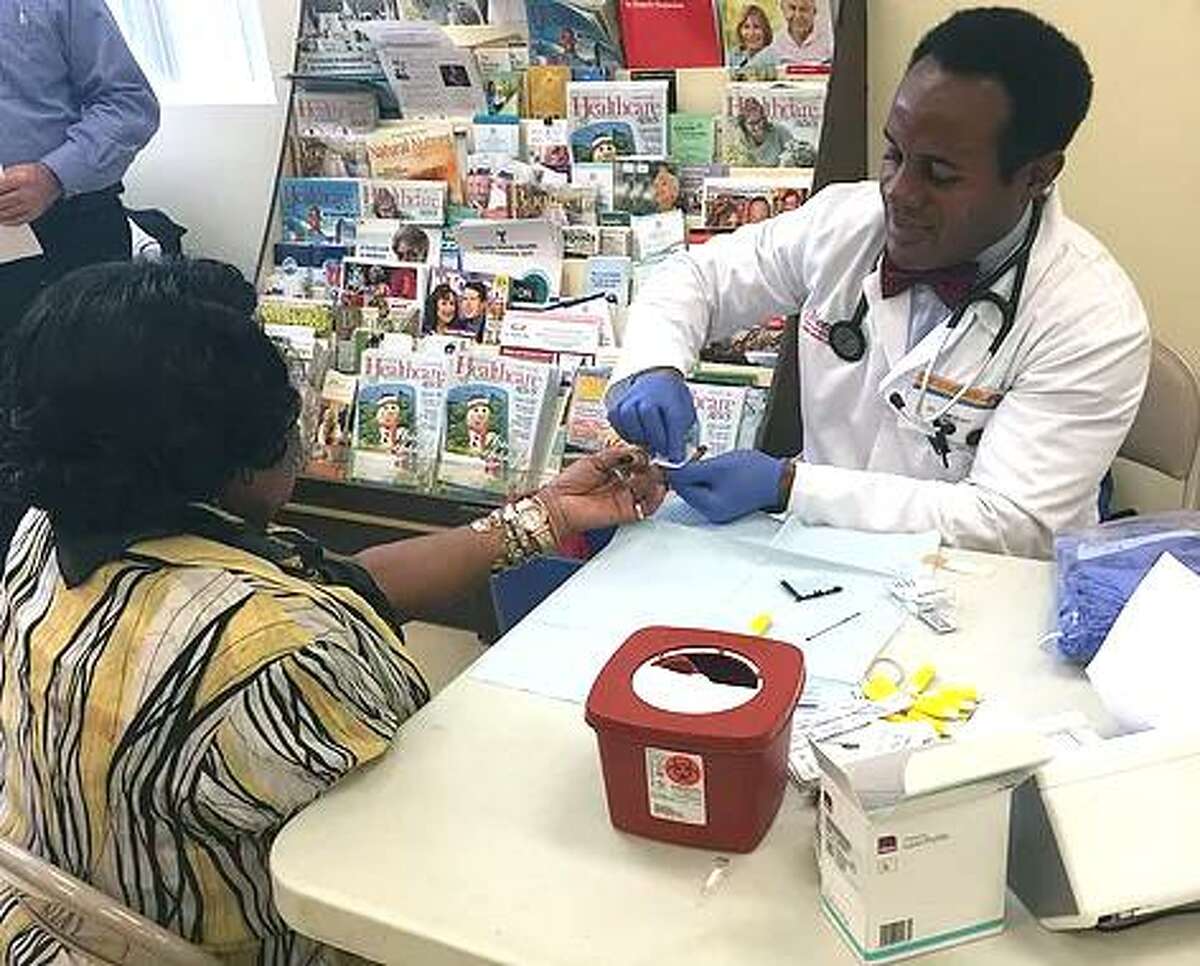 A photograph from the Bridging the Gap Education, Inc. website shows Dr. Noel Kayo performing high blood pressure and diabetes screenings with seniors citizens in Bridgeport.