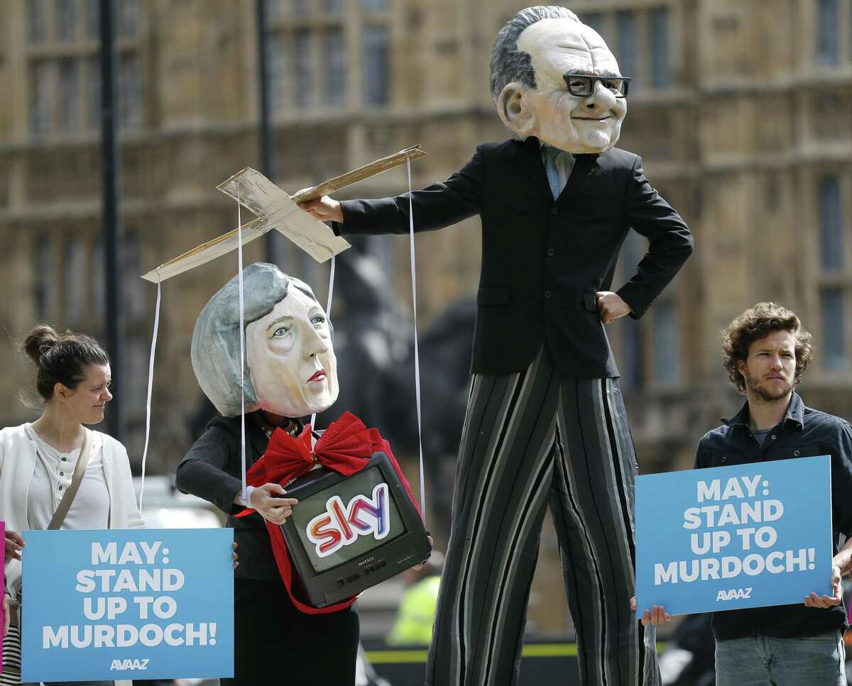 Campaigners from the community-based organization Avaaz, wearing a mask of Rupert Murdoch (right), and Prime Minister Theresa May, stage a protest opposite parliament in London on Thursday. British authorities Thursday asked regulators to further examine 21st Century Fox’s deal for the European satellite giant.