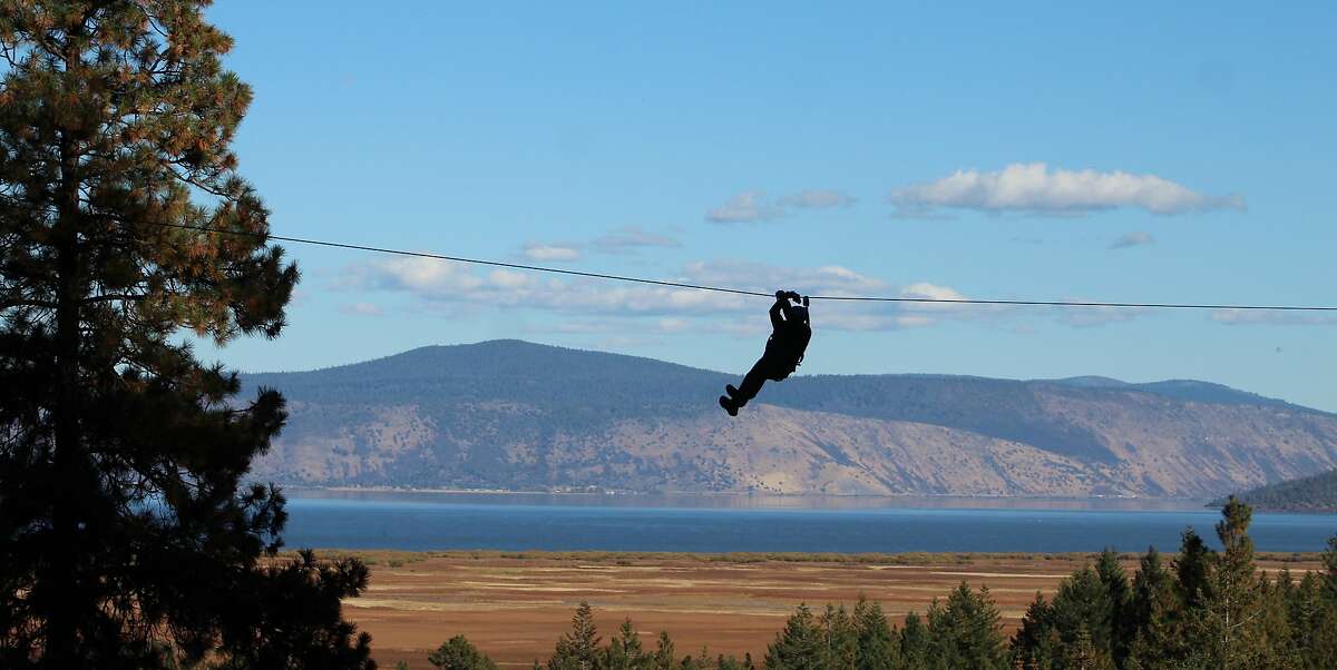 Chronicle outdoors writer Tom Stienstra rides the zipline over a break in the forest canopy with Klamath Lake in the background.