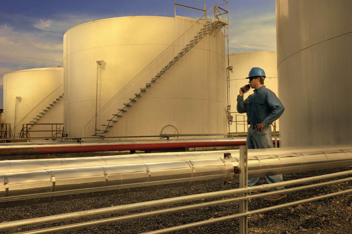 A man stands next to storage tanks at an oil refinery in this Getty stock image. 