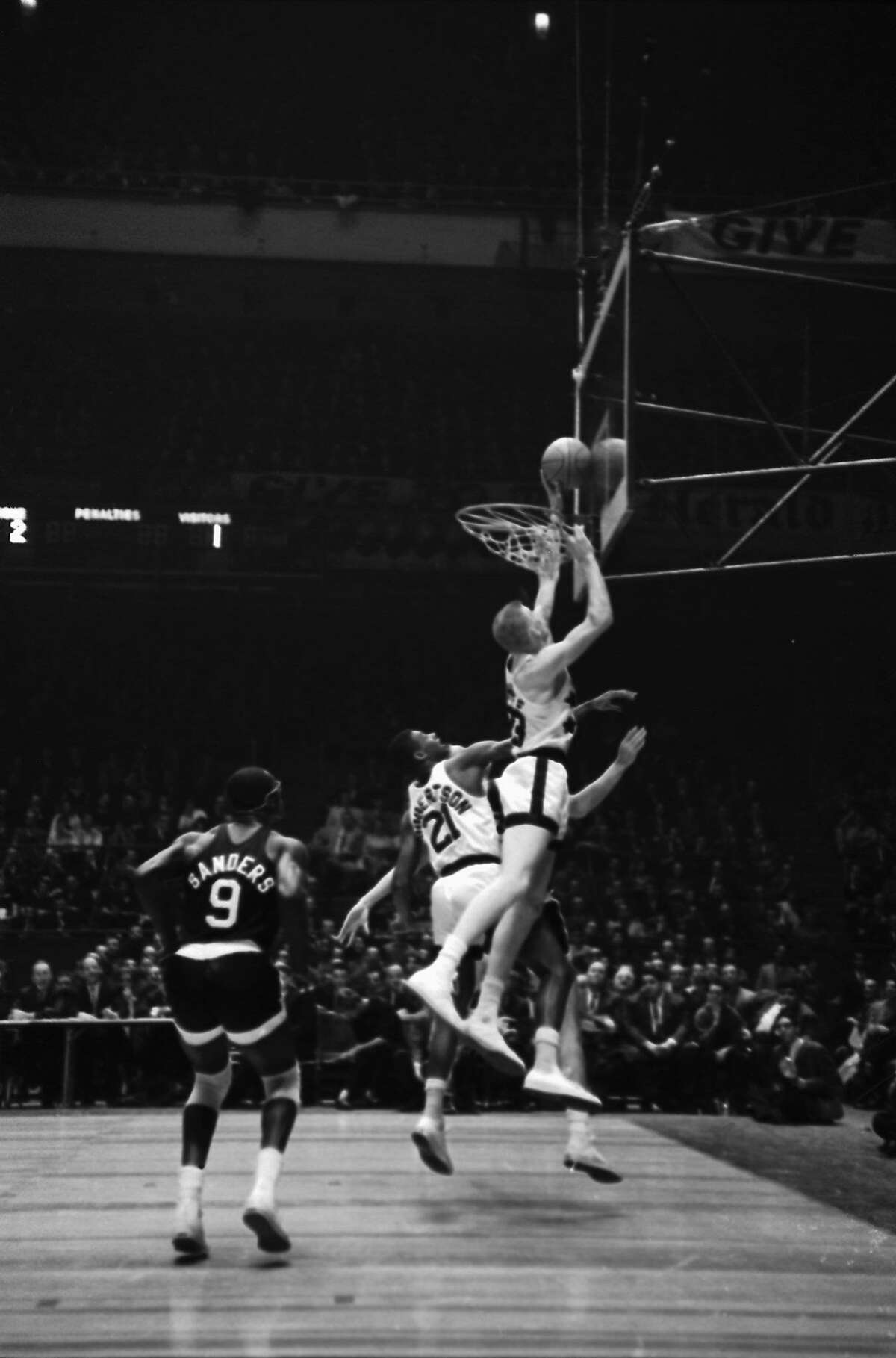 (Original Caption) In a burst of over-enthusiasm, Darrell Imhoff, of the University of California, reaches through the hoop to snare the ball as Oscar Robertson (no. 21), of the University of Cincinnati, watches. Goaltending was called on the play during the East-West All-Star game here, March 26th. The East All-Stars scored a close 67-66 victory over the West.