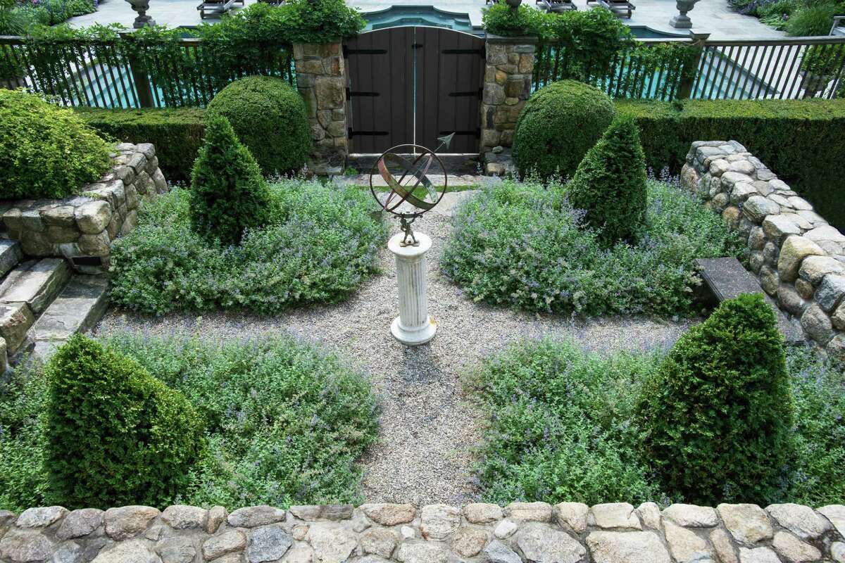 A formal garden is surrounded by a fieldstone wall just outside the gate into the pool area.