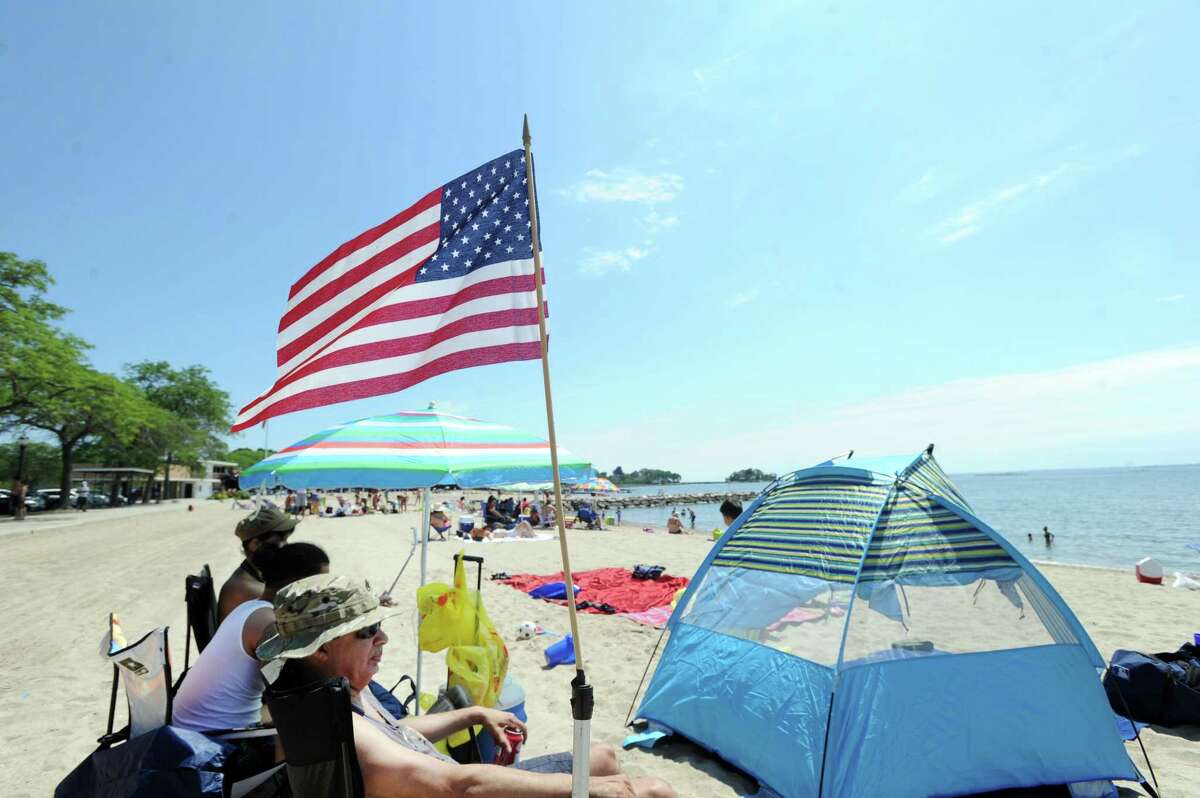 At left, Ben Marrero of the Bronx, N.Y., flew an American Flag that was attached to his beach chair while enjoying the beautiful weather with friends on the Fourth of July at Cummings Park beach in Stamford, Conn., Tuesday, July 4, 2017.
