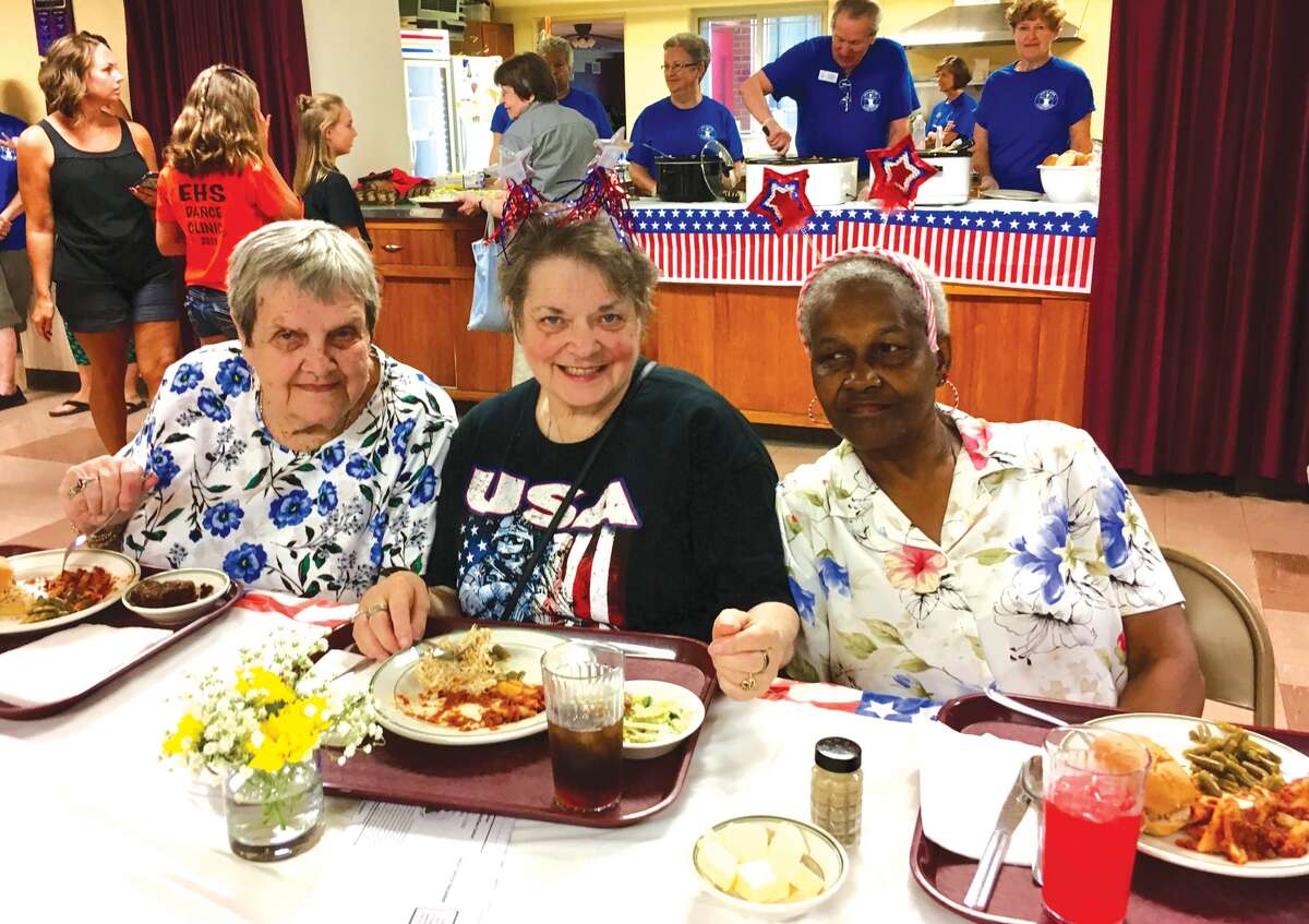 Eating lunch recently at Immanuel United Methodist Church are, from left, Kathy Erspamer, Linda Dillon and Mary Nunn. Faith in Action volunteers are serving meals behind them.