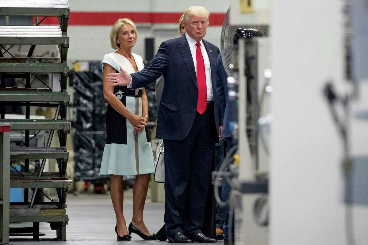 FILE - In this June 13, 2017, file photo, President Donald Trump, accompanied by Education Secretary Betsy DeVos, left, waves to members of the media as he takes a tour of Waukesha County Technical College in Pewaukee, Wis. Democratic attorneys general in 18 states and the District of Columbia are suing Education Secretary Betsy DeVos over her decision to suspend rules meant to protect students from abuses by for-profit colleges. The lawsuit was filed Thursday, July 6, 2017, in federal court in Washington and demands implementation of borrower defense to repayment rules. (AP Photo/Andrew Harnik, File)