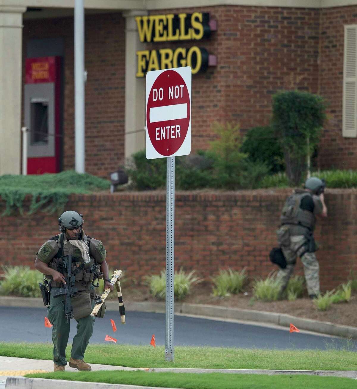 Police officers move away from a Wells Fargo Bank, Friday, July 7, 2017 in Marietta, Ga. A man who claimed to have a bomb that could "take out the room" barricaded himself inside a suburban Atlanta bank Friday, sparking an hours-long standoff that forced police to bust through a brick wall of the building and later ended with the suspect's death.(AP Photo/Mike Stewart)