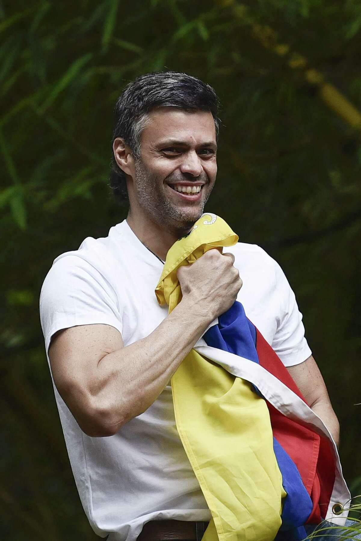 Opposition leader Leopoldo Lopez holds a Venezuelan flag as he arrives home Saturday after being released from a military prison in Caracas, Venezuela. ﻿
